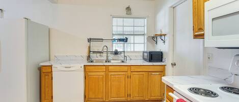 A compact kitchen with wooden cabinets, a white refrigerator, a microwave, and a stove.