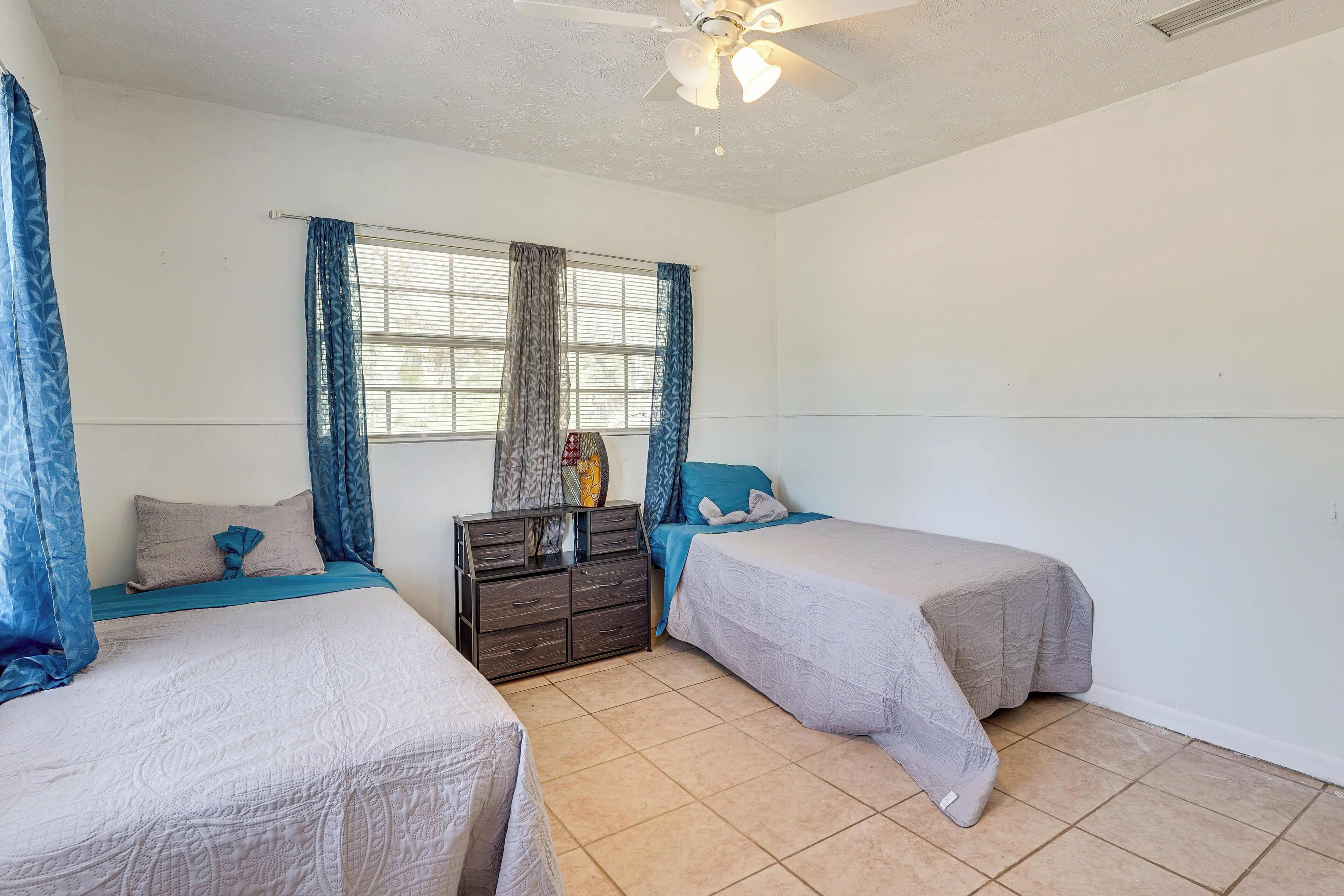 A bedroom with two beds, a dresser, and a ceiling fan.