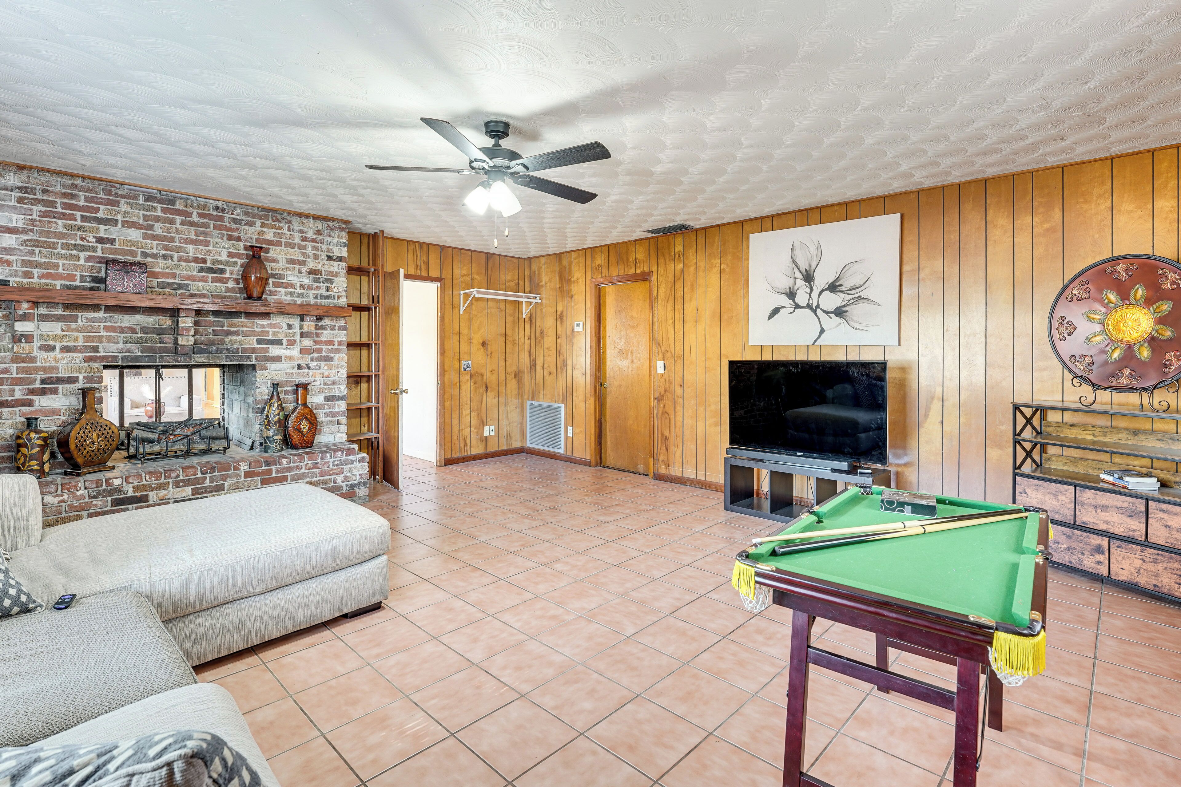 A living room with a brick fireplace, a pool table, a sofa, and a television.
