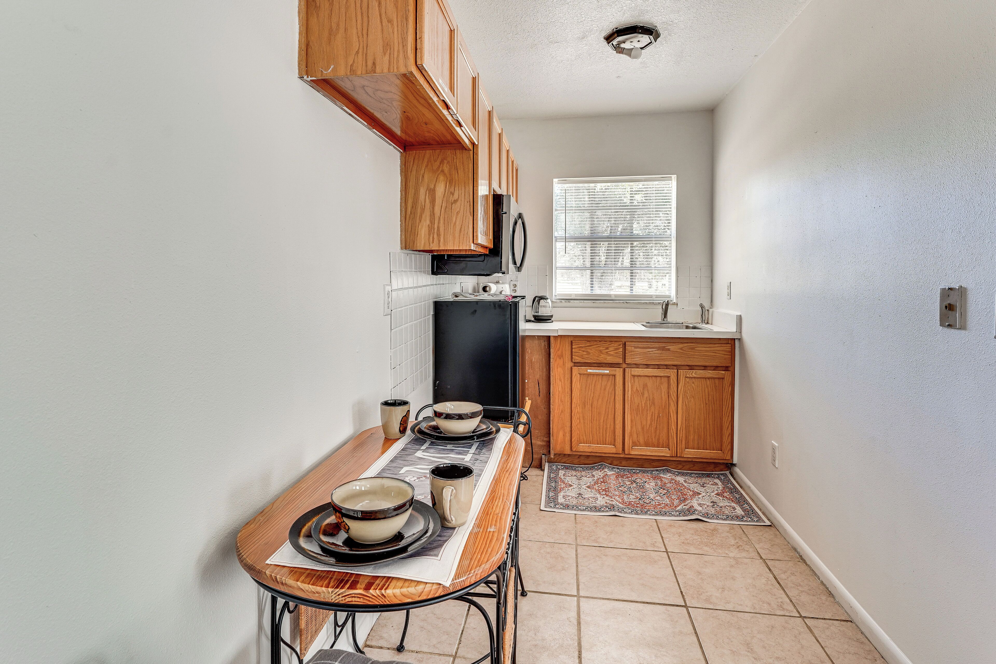 A compact kitchen with wooden cabinets, a microwave, and a dining area with a table set for two.