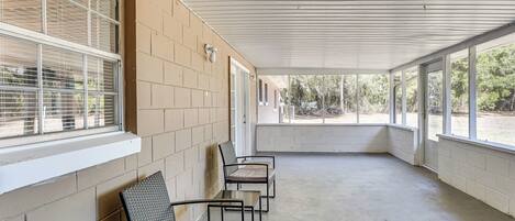 A covered outdoor seating area with four chairs and a table, beige brick walls, and large windows.