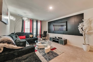 A modern living room with a black sofa, a glass coffee table, a flat-screen TV mounted on the wall, and a potted white orchid plant. - Group Haven in Princeton! WFH Ready & Ample Space (Princeton)