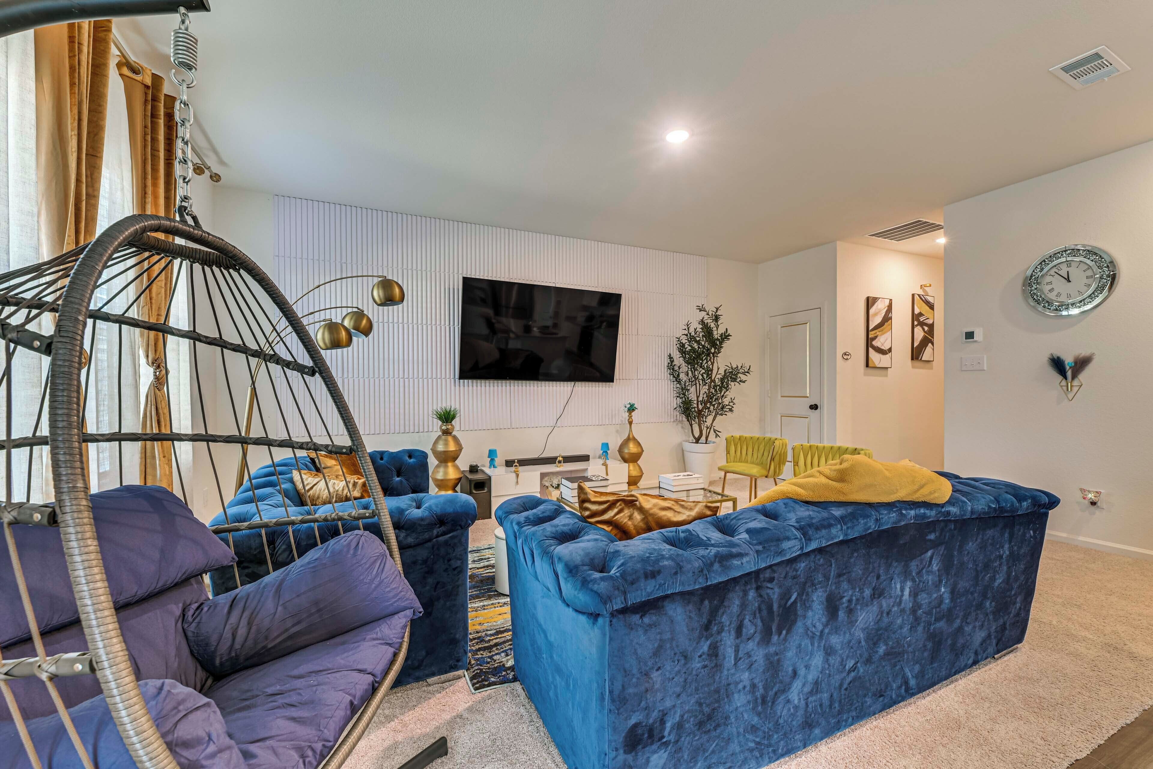 A modern living room with a hanging chair, a blue sofa, and a flat-screen TV mounted on the wall.