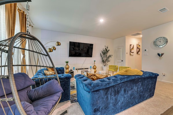 A modern living room with a hanging chair, a blue sofa, and a flat-screen TV mounted on the wall. - Group Haven in Princeton! WFH Ready & Ample Space (Princeton)