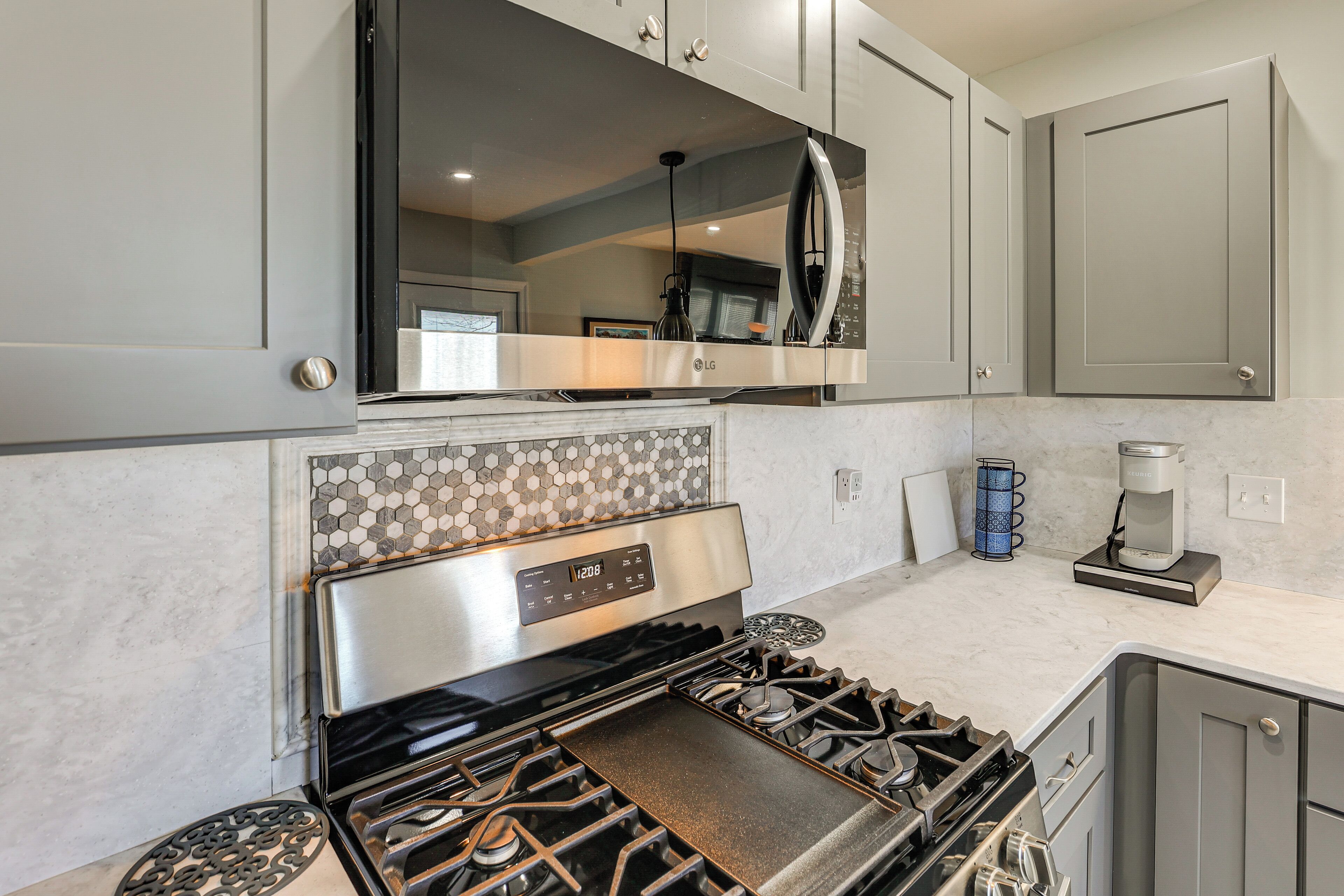 A modern kitchen with a stainless steel stove, grey cabinets, and a tiled backsplash.