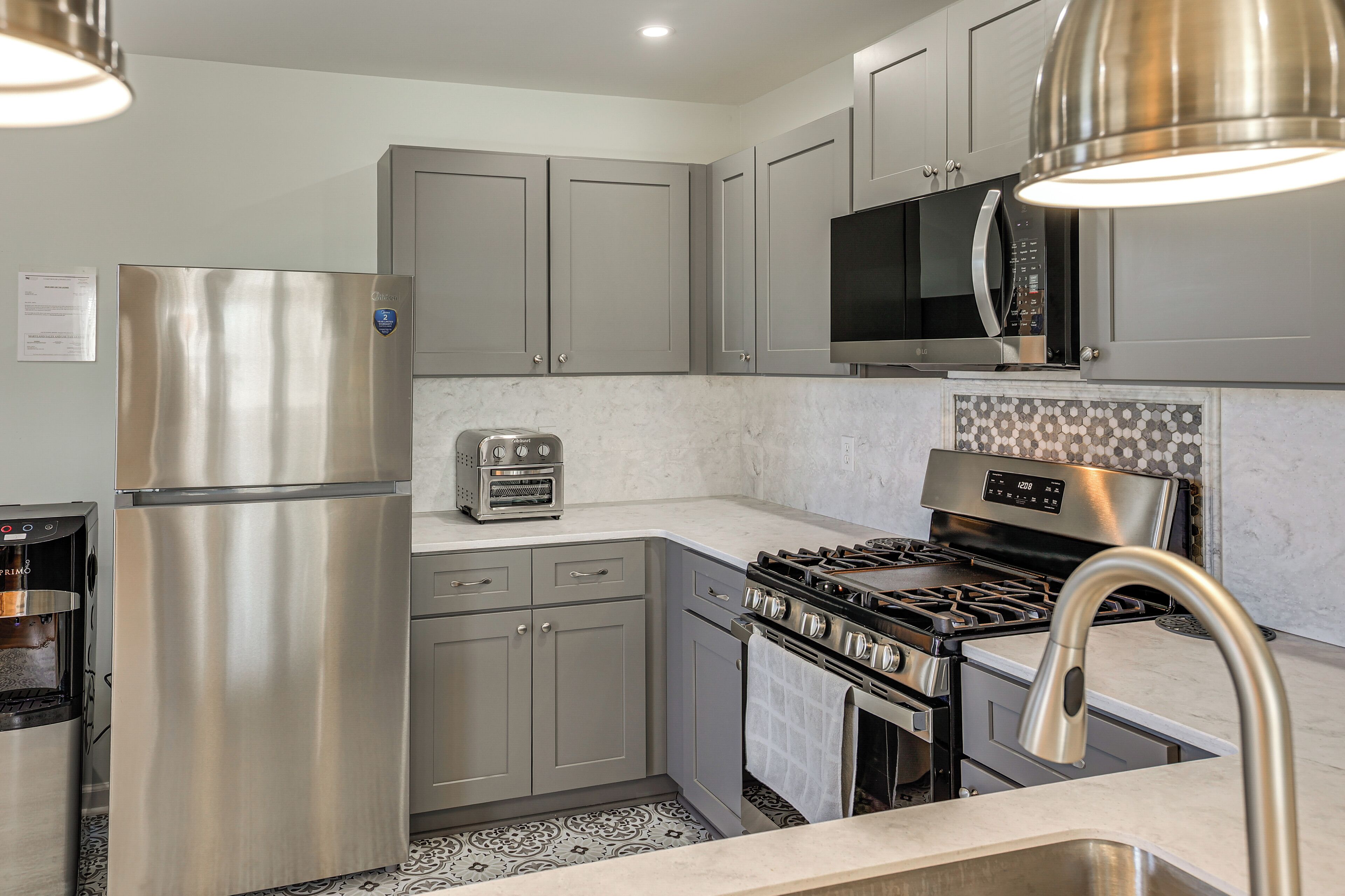 A modern kitchen with stainless steel appliances, grey cabinets, a built-in microwave, and a patterned backsplash.