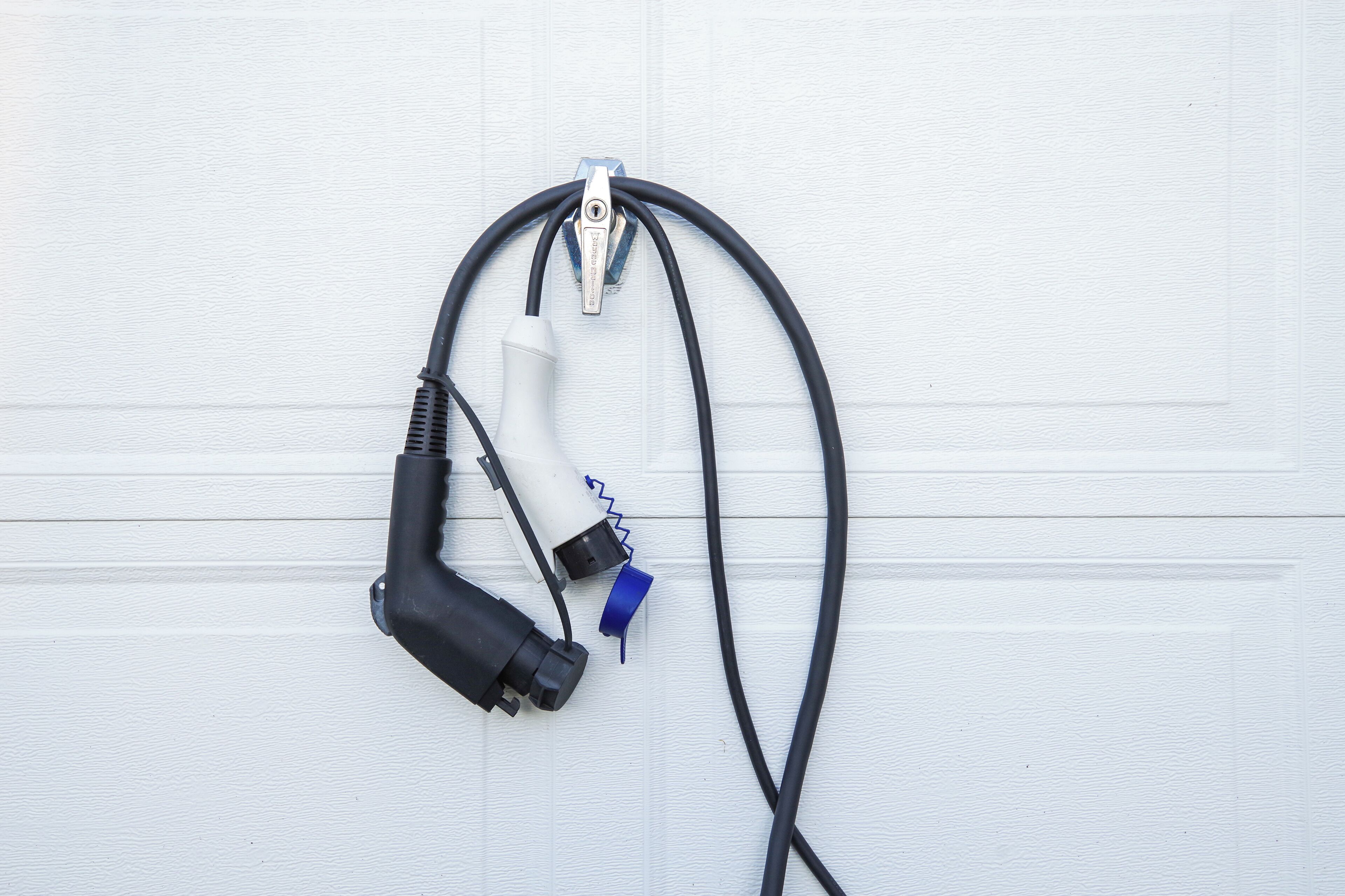 Paredes brancas com um cabo elétrico preto e um dispositivo branco com conector azul.