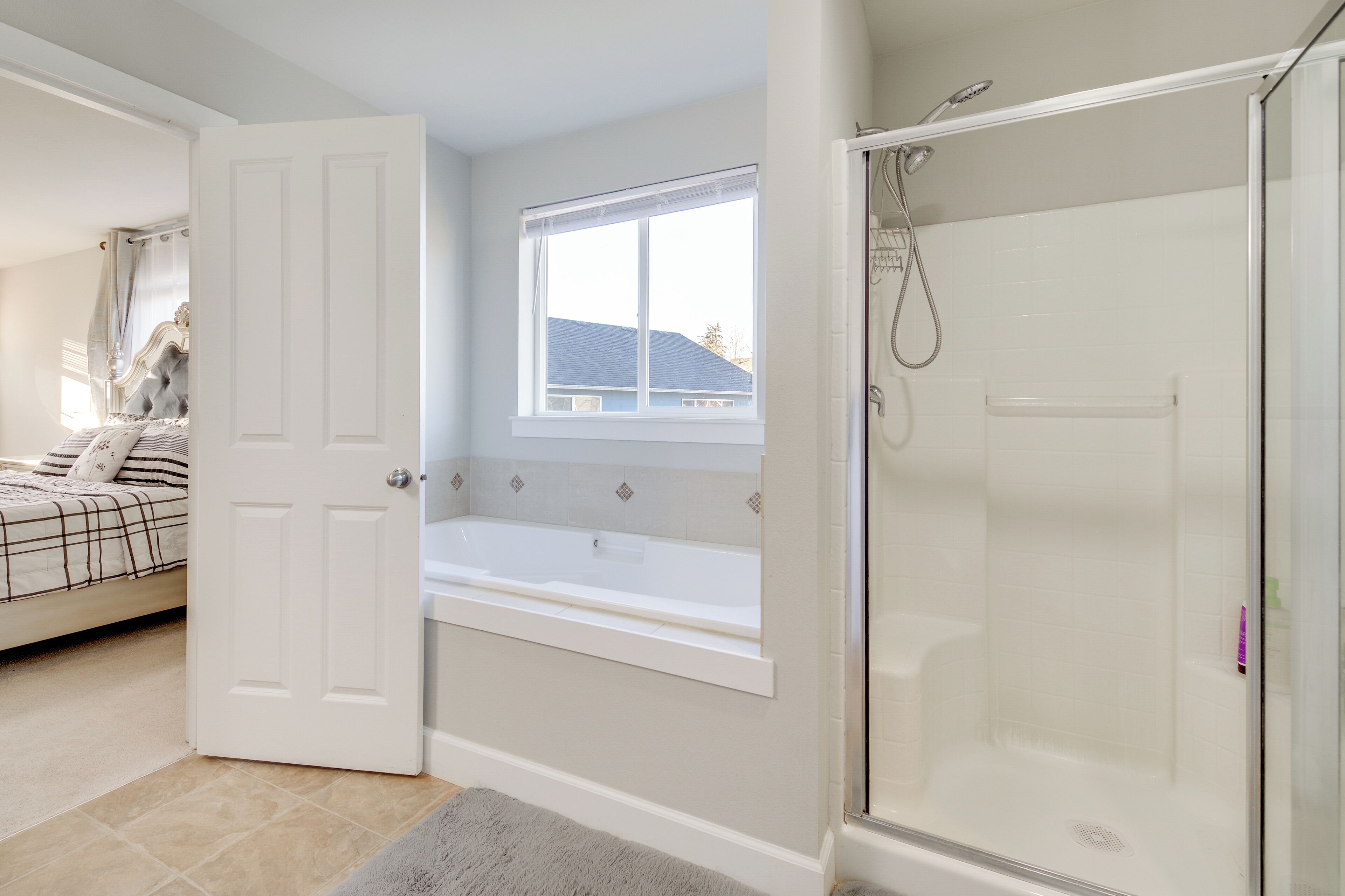 A bedroom with a bed, a window, a bathtub, and a shower.