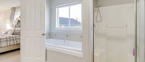 A bedroom with a bed, a window, a bathtub, and a shower.