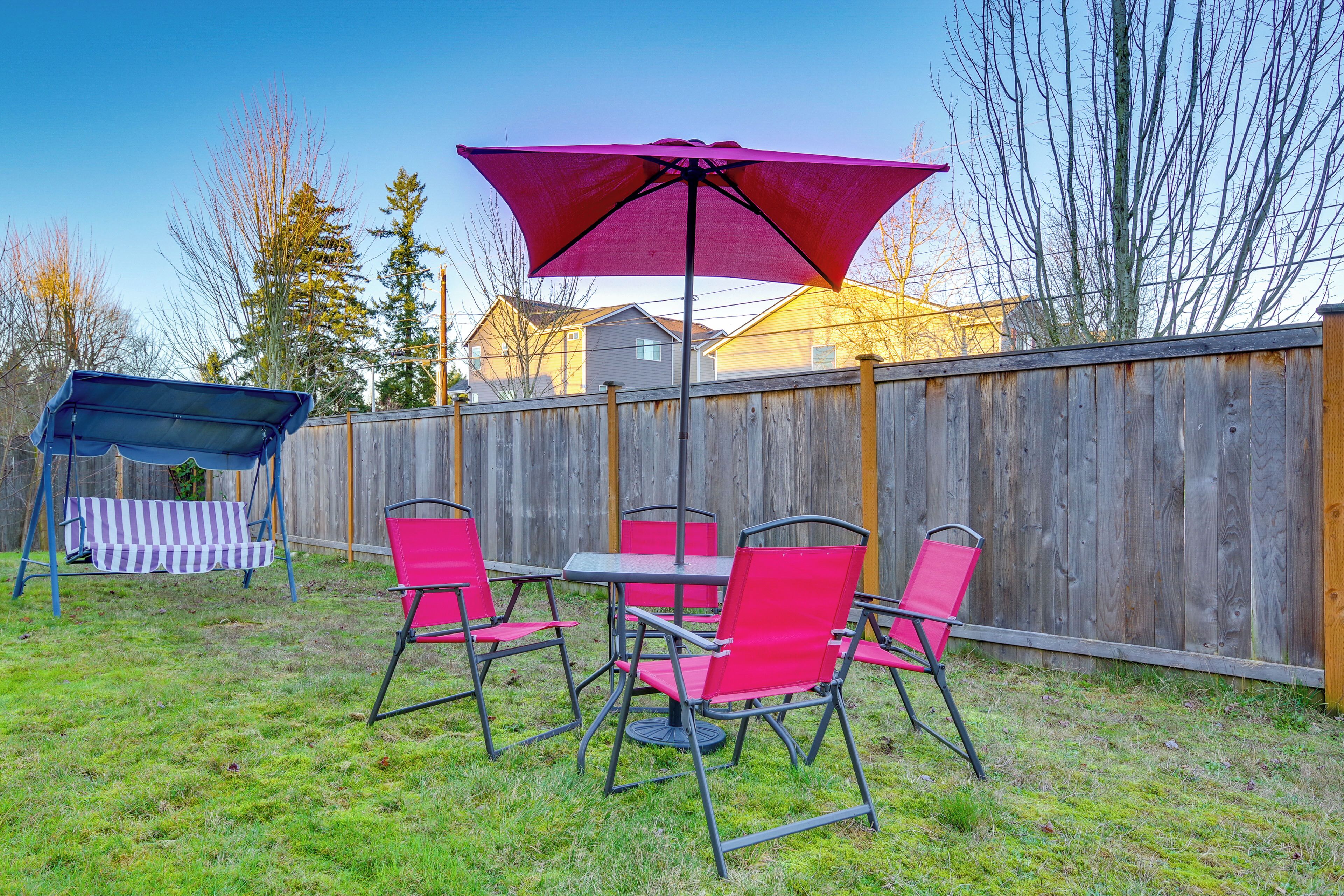 A backyard with a wooden fence, a table with chairs, and a large umbrella.