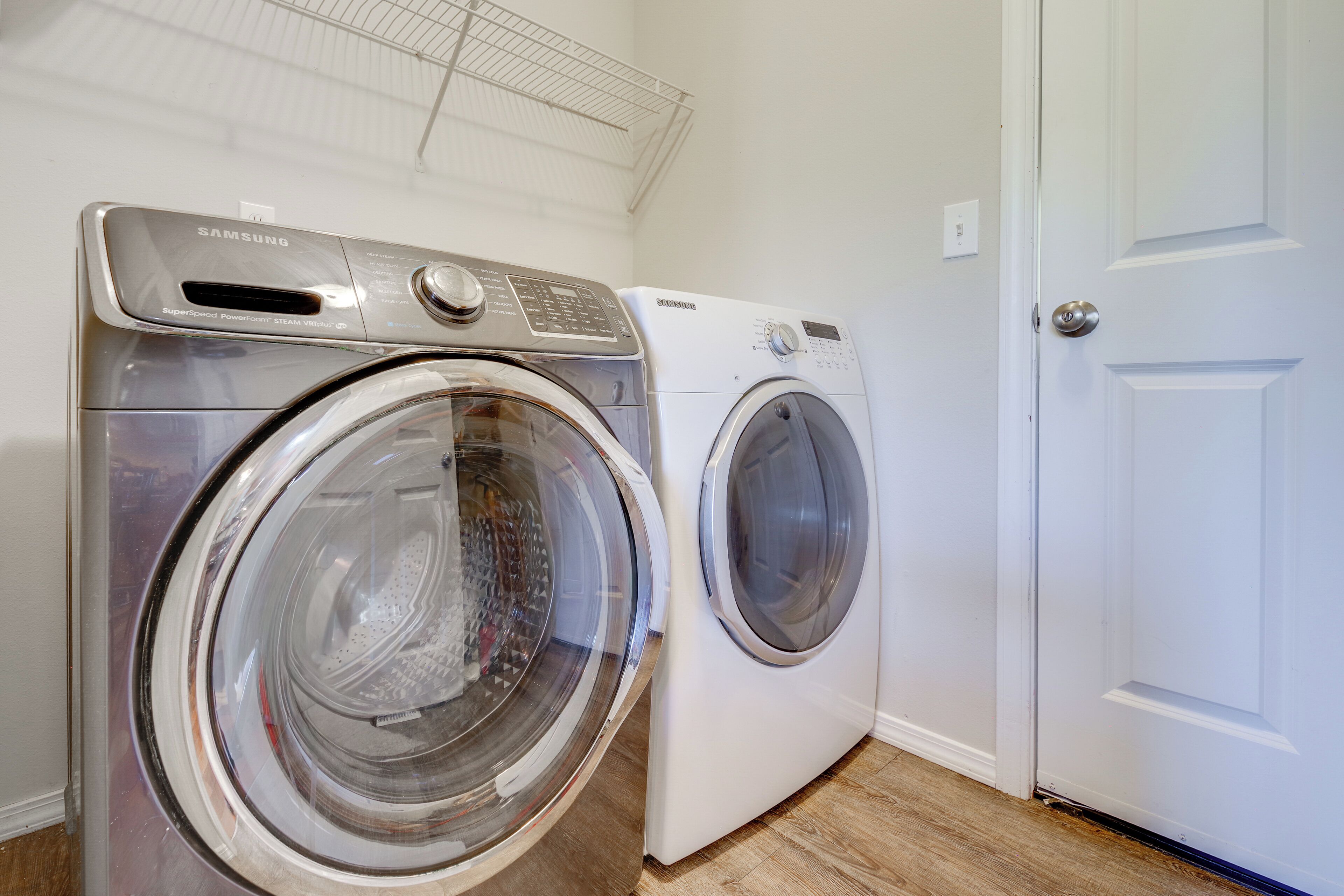 A laundry room with two front-loading washing machines, a white door, and a metal shelf above the machines.