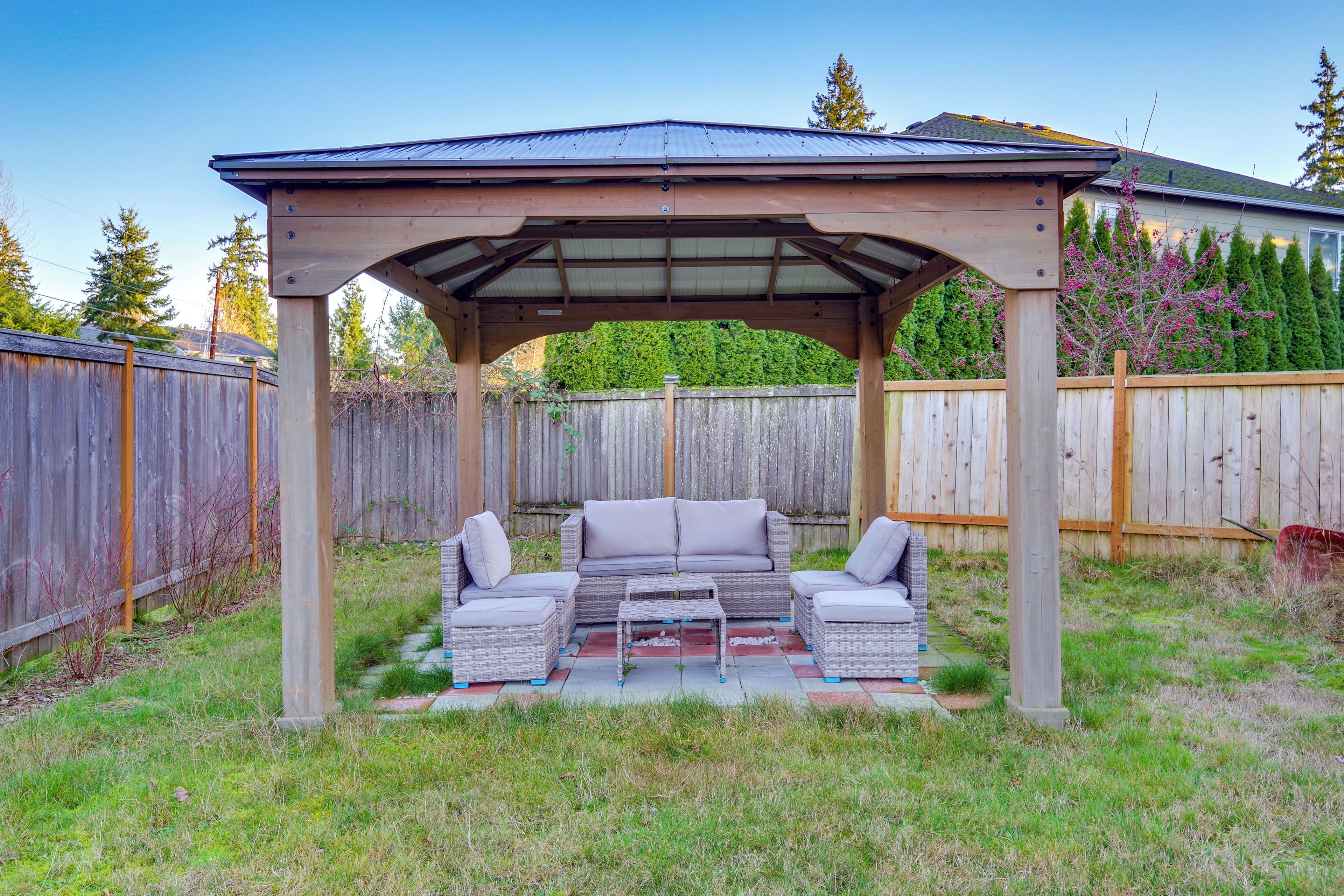 A covered outdoor seating area with a sofa and chairs, a small table, and a pergola structure.