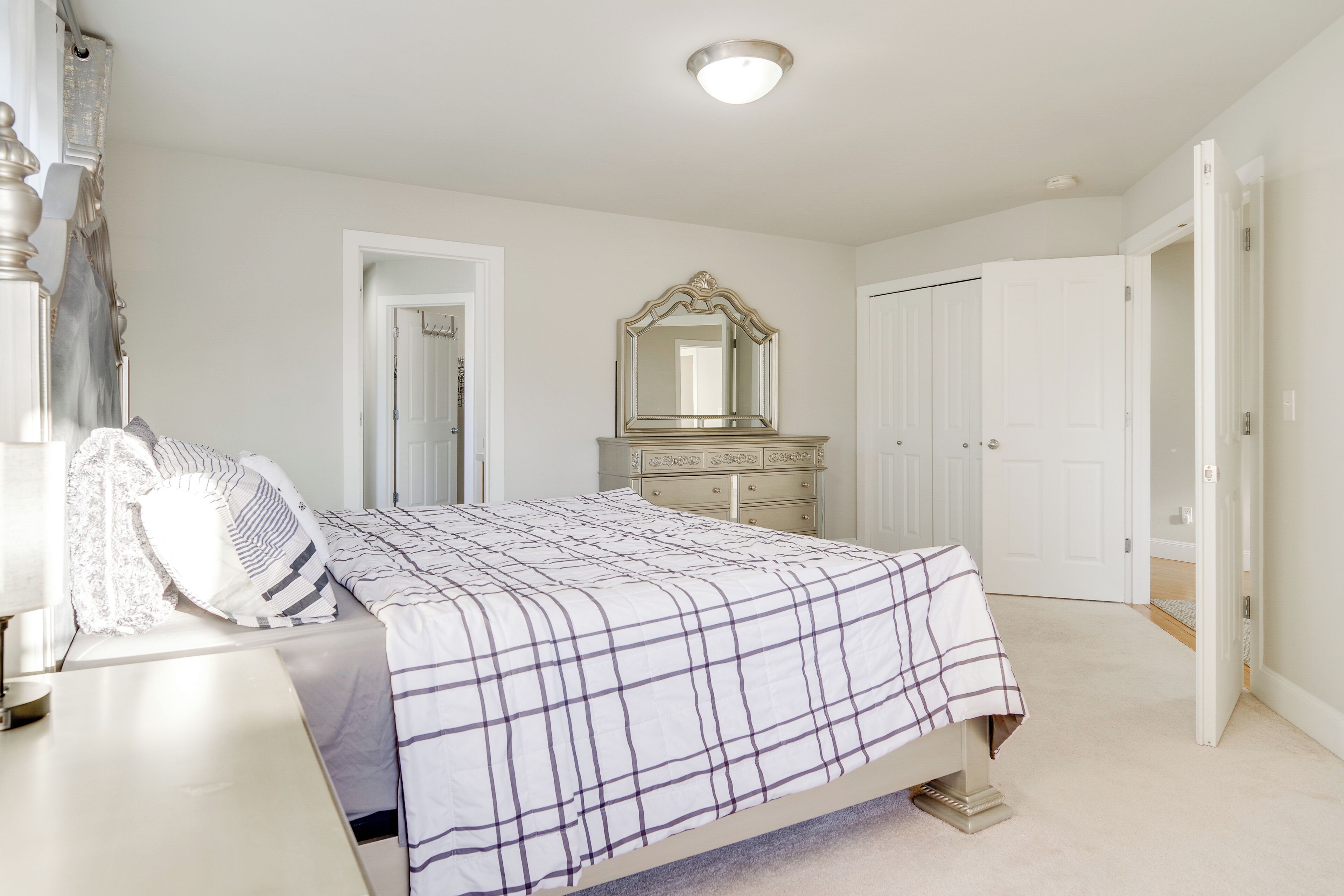 A bedroom with a bed, dresser, mirror, and two doors.