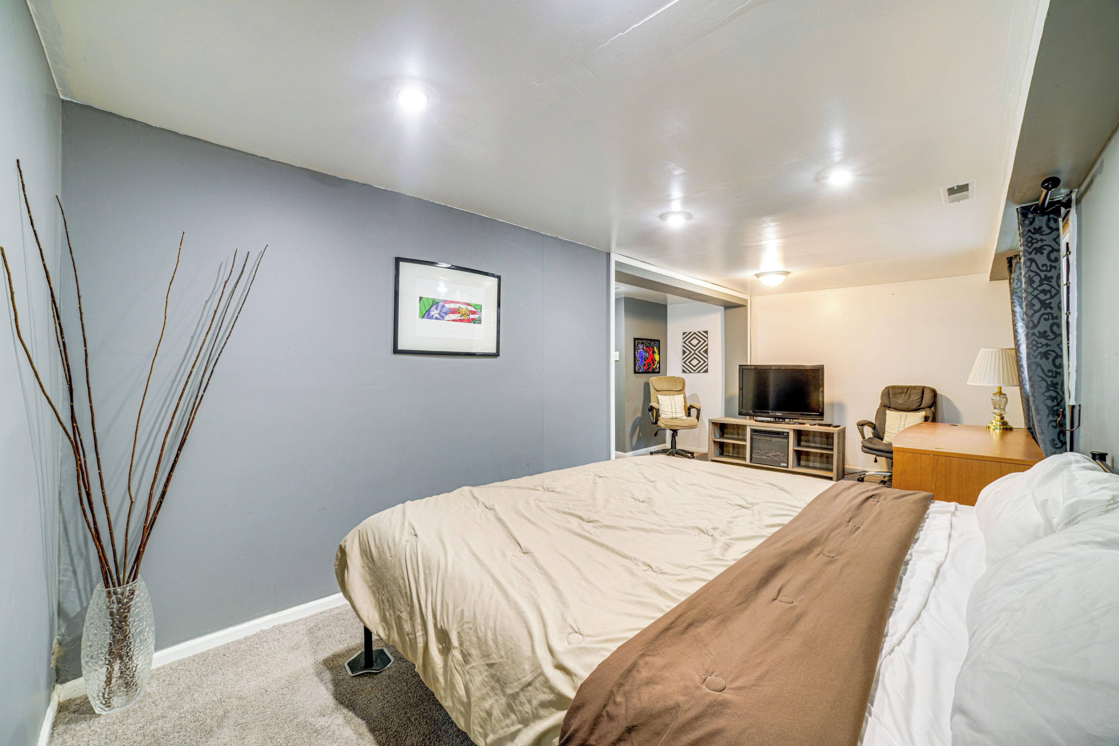 A modern hotel room with a large bed, a television, a desk with a lamp, and a vase with branches.
