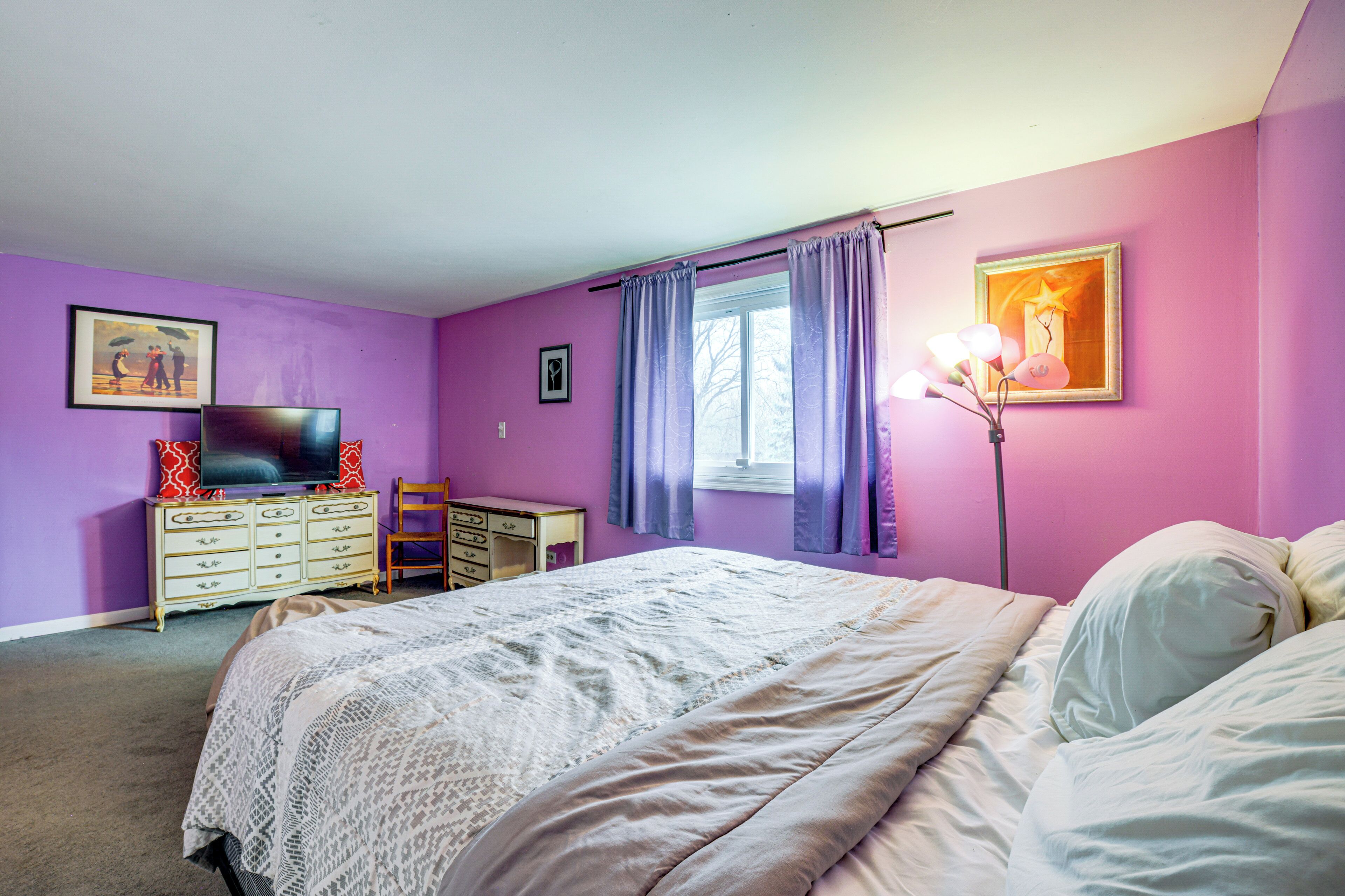 Une chambre à coucher comprenant un lit, une commode, un téléviseur et deux tableaux encadrés accrochés au mur.