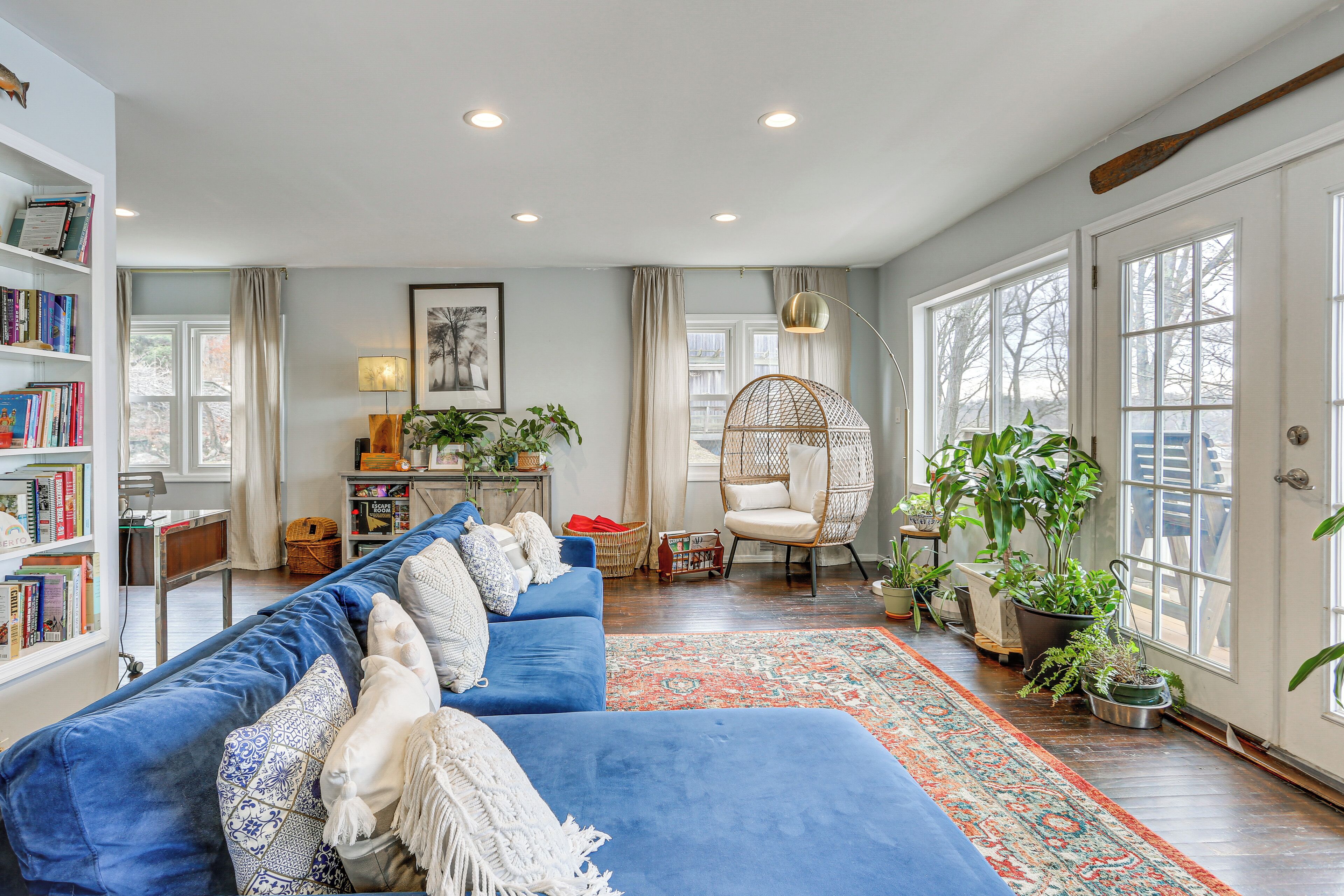 A spacious living room with a blue sofa, a wicker chair, and a large window.