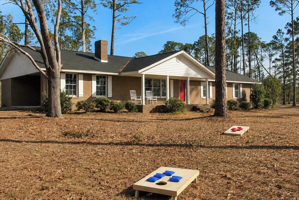 A two-story house with a porch, a covered outdoor seating area, and a wooden table with blue cushions.