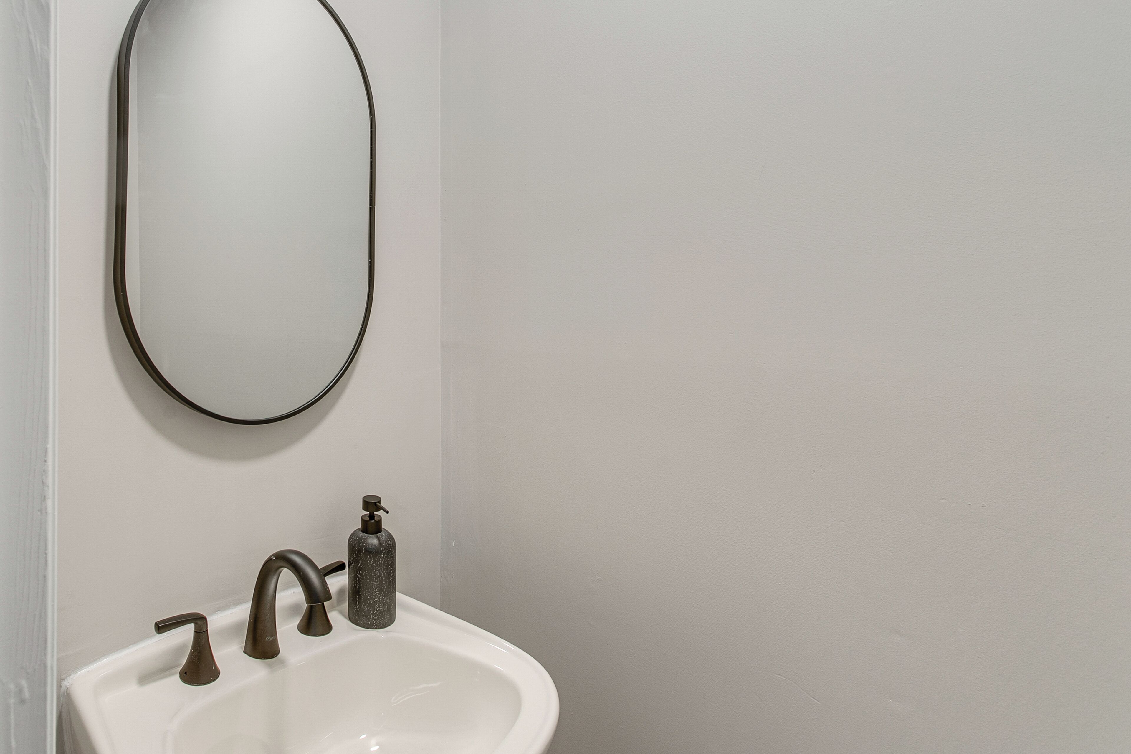 Een badkamer met een witte wastafel, twee kranen en een zeepdispenser.
