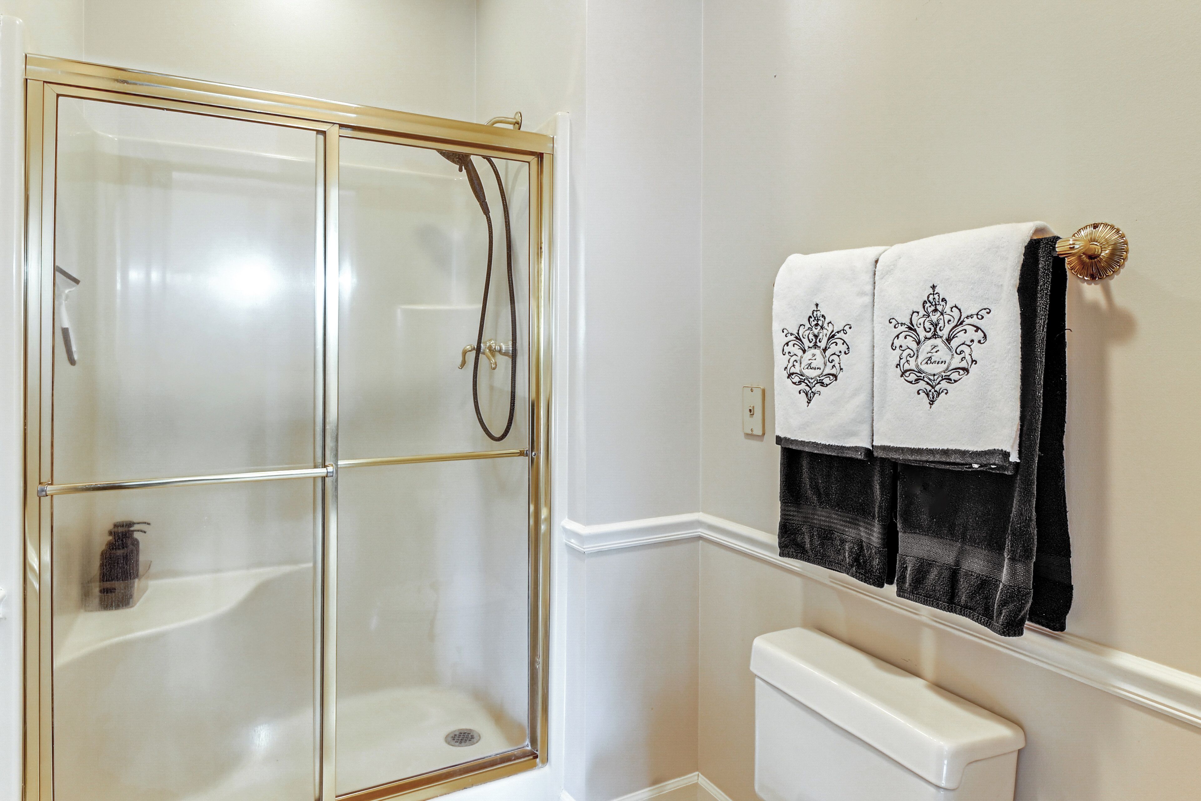 A bathroom with a glass-enclosed shower, a white toilet, and two towels hanging on a rack.