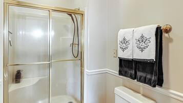 A bathroom with a glass-enclosed shower, a white toilet, and two towels hanging on a rack.