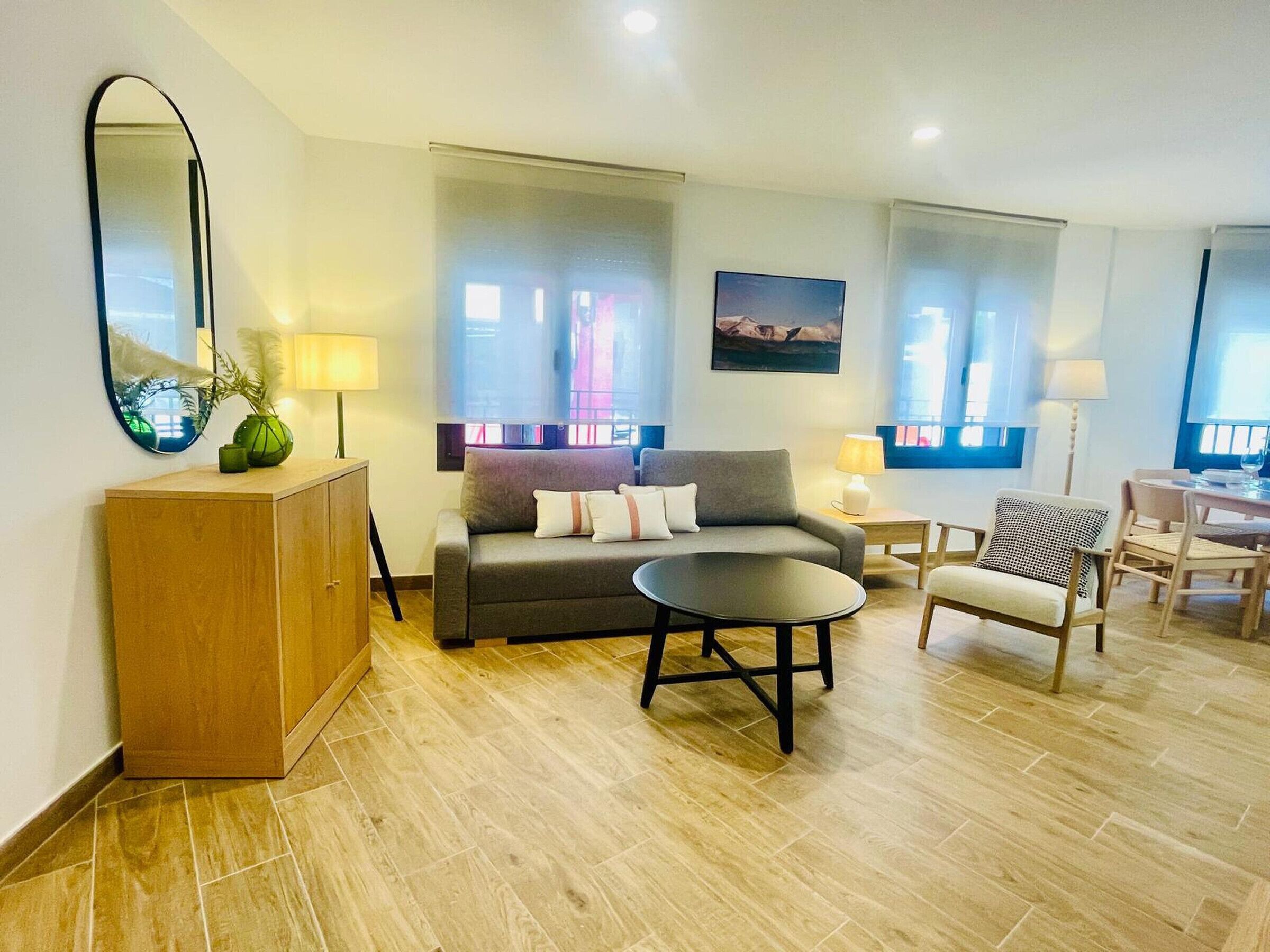 A modern living room with a sofa, a coffee table, a wooden cabinet, and a dining area with chairs and a table.