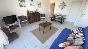 A living room with a sofa, TV, wooden cabinet, and a bench. - Charming 1-Bedroom with Balcony, Parking Included, Close to Beach & Shops (Arcachon)