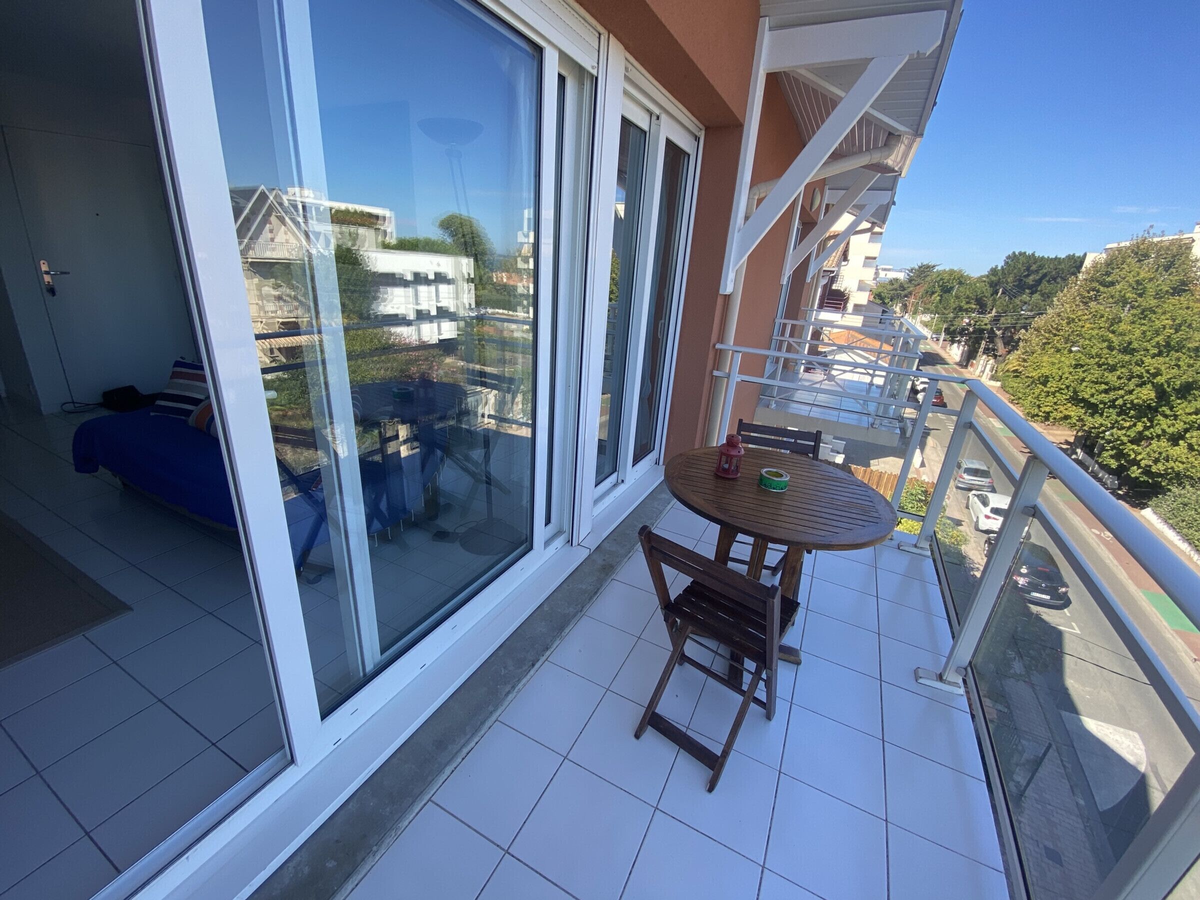 A balcony with a table and chairs, a bed, and a view of the street and buildings.