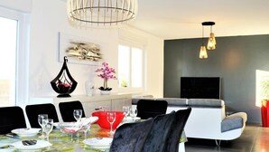 Et moderne spiseområde med et bord til fire, en sofa og et fjernsyn i baggrunden.