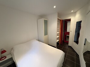 A bedroom with a bed, a wardrobe, a red lamp, and a bathroom with a shower curtain. - Air-conditioned villa with parking for 2 people in Cap d'Agde (Cap d'Agde)