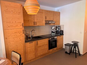 Une cuisine avec des meubles de rangement en bois, un plan de travail noir, un évier en acier inoxydable, un four à micro-ondes, un grille-pain et une poubelle.