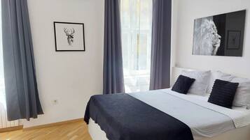 A bedroom with a bed, grey curtains, a framed deer picture, and a white wall.