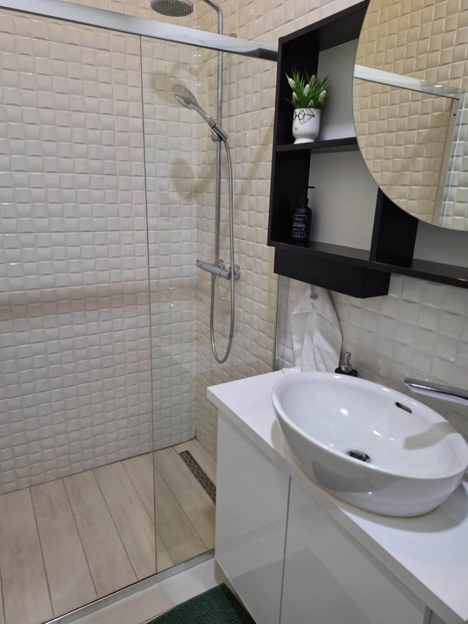 Un baño moderno con ducha de vidrio, un lavabo blanco y un espejo sobre el lavabo.