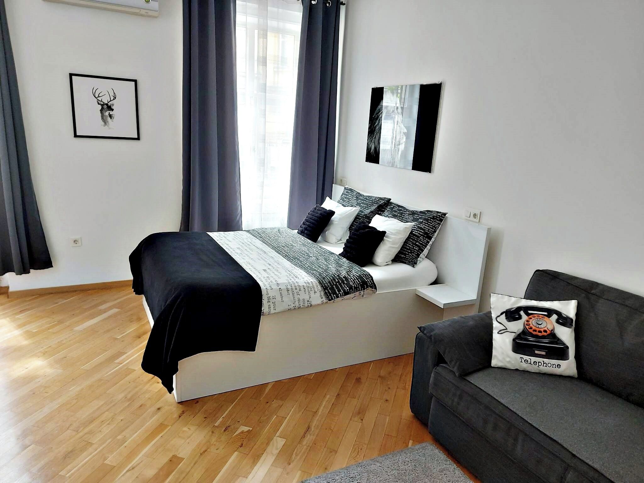 A modern bedroom with a bed, a grey sofa, and a window with curtains.
