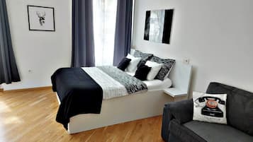 A modern bedroom with a bed, a grey sofa, and a window with curtains.