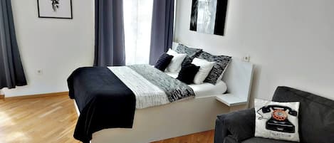 Een moderne slaapkamer met een bed, een grijze bank en een raam met gordijnen.
