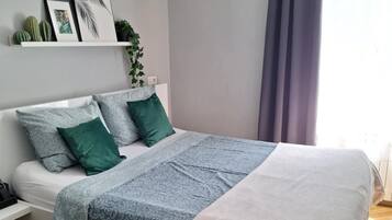 Un dormitorio ordenado con cama, almohadas, una mesita de noche y una estantería decorada.