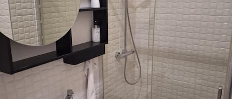 A modern bathroom with a white sink, a round mirror, and a glass-enclosed shower.