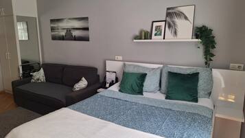 Et moderne soveværelse med seng, sofa, et natbord og en vægmonteret hylde med pynt.