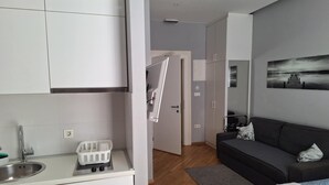 Ett kompakt hotellrum med ett litet kök, en soffa, en säng och en tavla på väggen.