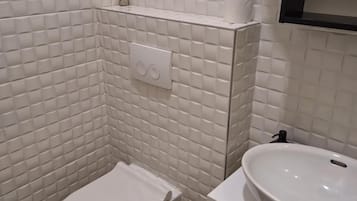 A modern bathroom with white tiles, a toilet, a sink, and a towel rack.
