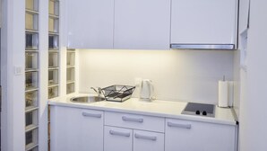 Ett modernt kök med vita skåp, en diskho i rostfritt stål, en vattenkokare och en svart korg av metall på bänkskivan.