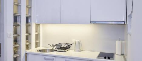 Una cocina moderna con armarios blancos, un lavamanos de acero inoxidable, un hervidor y una cesta de alambre negra sobre la encimera.