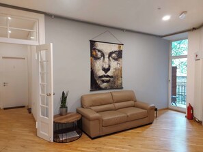 A room with a beige leather sofa, a wooden coffee table, a potted plant, and a large abstract painting on the wall. - Spin&Fly (Zagreb)