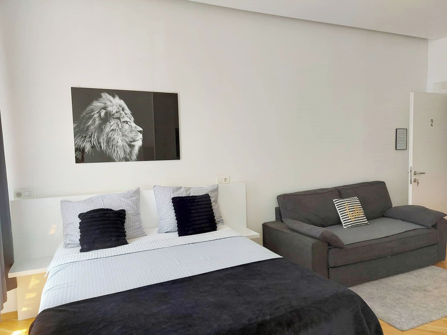 A modern bedroom with a bed, a grey sofa, and a framed picture on the wall.