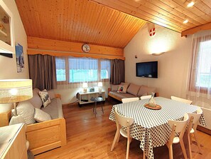 A cozy living room with a wooden ceiling, a sofa set, a dining table with chairs, and a flat-screen TV mounted on the wall. - Charming 2-room apartment in Méribel, 4 people, near slopes (Méribel)