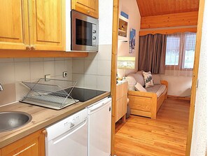 A compact kitchen with wooden cabinets, a microwave, a dishwasher, and a small dining area with a table and chairs. - Charming 2-room apartment in Méribel, 4 people, near slopes (Méribel)