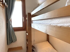 Ein Stockbett mit Fenster, Vorhängen und einem Holzregal.