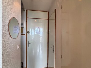 Ein Zimmer mit einer weißen Tür, einem kleinen Spiegel und einer Wandleuchte.
