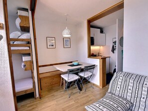 Ein kleines Zimmer mit Etagenbett, Schreibtisch mit Stuhl, einer Küchenzeile und einer Couch.
