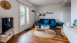 Un salon moderne avec un canapé bleu, un téléviseur posé sur un meuble, une table d’appoint en osier et un tapis rond.
